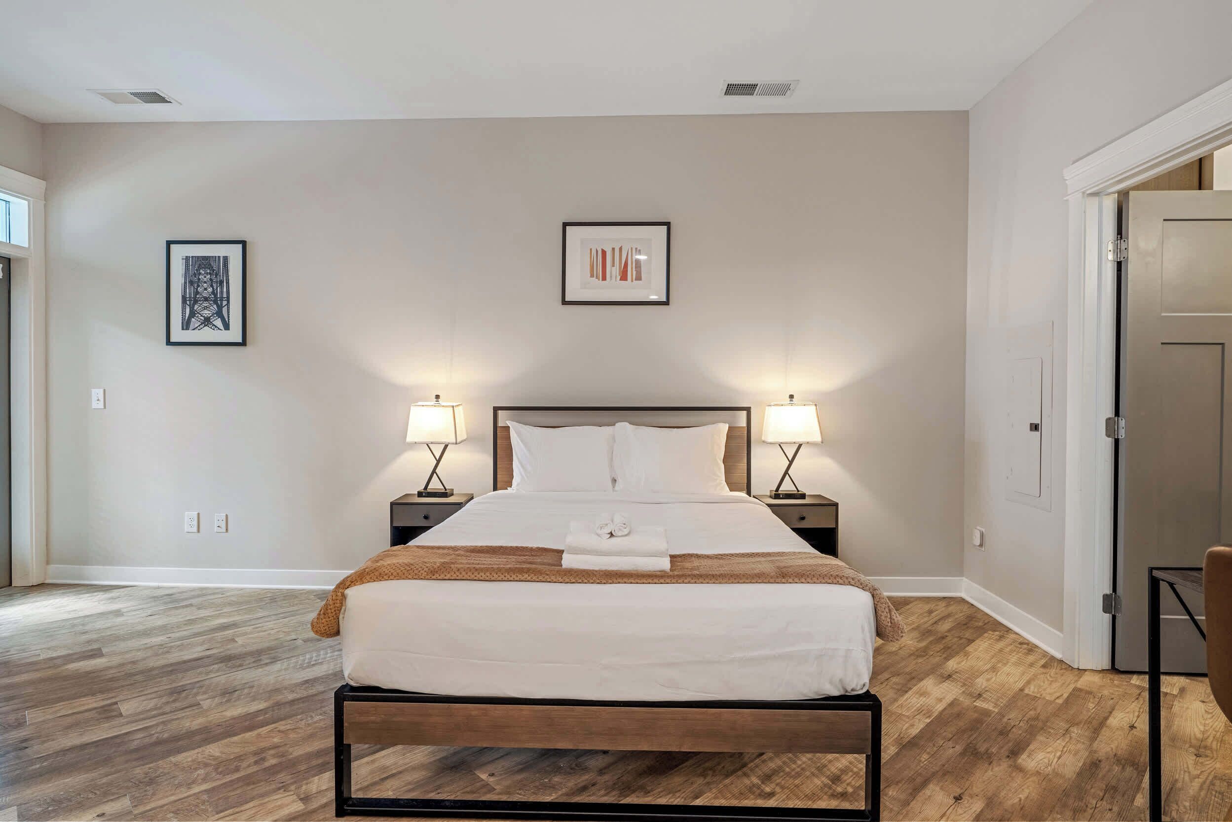 Une chambre à coucher bien rangée, avec un lit, deux tables de chevet et deux lampes fixées au mur.