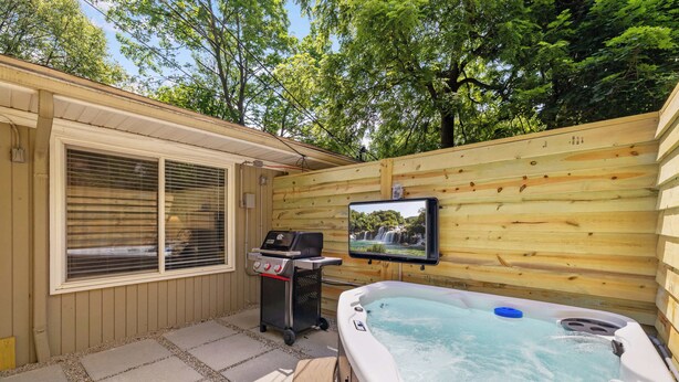 A hot tub in a wooden deck area with a TV screen mounted on the wall.
