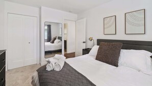 A modern bedroom with a bed, a nightstand, a mirror, and two framed artworks on the wall.