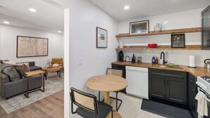 A modern kitchen with dark cabinets, a wooden countertop, and a sink. There is a dining area with a round table and chairs.