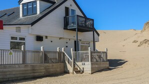 A white building with a balcony, wooden fence, and a staircase leading to a door.