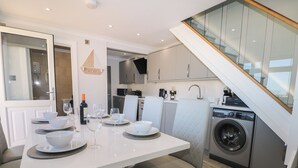 A modern kitchen with a built-in washing machine, a dining area with a white table set for four, and a staircase leading to an upper level.