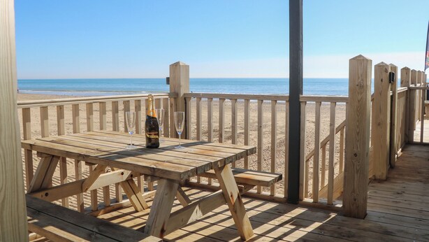 A wooden deck with a table and chairs, overlooking a beach.