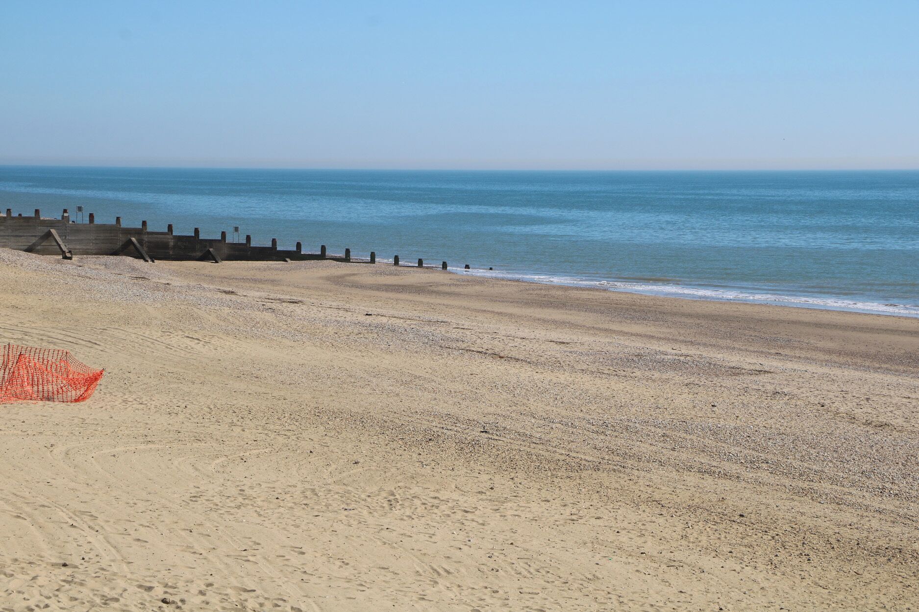 A beach with a sandy shore, a wooden breakwater, and a red safety net.