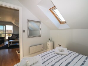Et soveværelse med ovenlys, et stort spejl, en radiator, et natbord og en seng med stribet sengetøj.