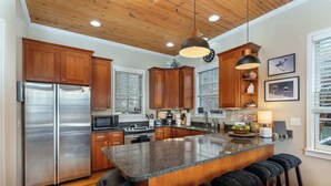 A modern kitchen with wooden cabinets, stainless steel appliances, a granite countertop, and a bar stool area. - 5 Min to Hatley Pointe~Hot Tub~Games~Dog Friendly (Mars Hill)