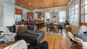 A spacious living room with a brown leather sofa, a dining area with a wooden table, and a kitchen with wooden cabinets and a stainless steel refrigerator. - 5 Min to Hatley Pointe~Hot Tub~Games~Dog Friendly (Mars Hill)