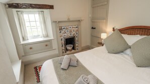 A bedroom with a bed, a window, a fireplace, and a nightstand with a lamp. - Old Cottage (Ulverston)