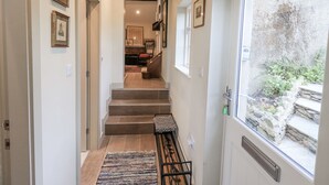 A hallway with a bench, framed pictures, and a view of a garden through a window. - Old Cottage (Ulverston)