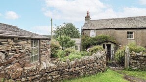 A stone cottage with a thatched roof, a stone wall, and a small garden. - Old Cottage (Ulverston)