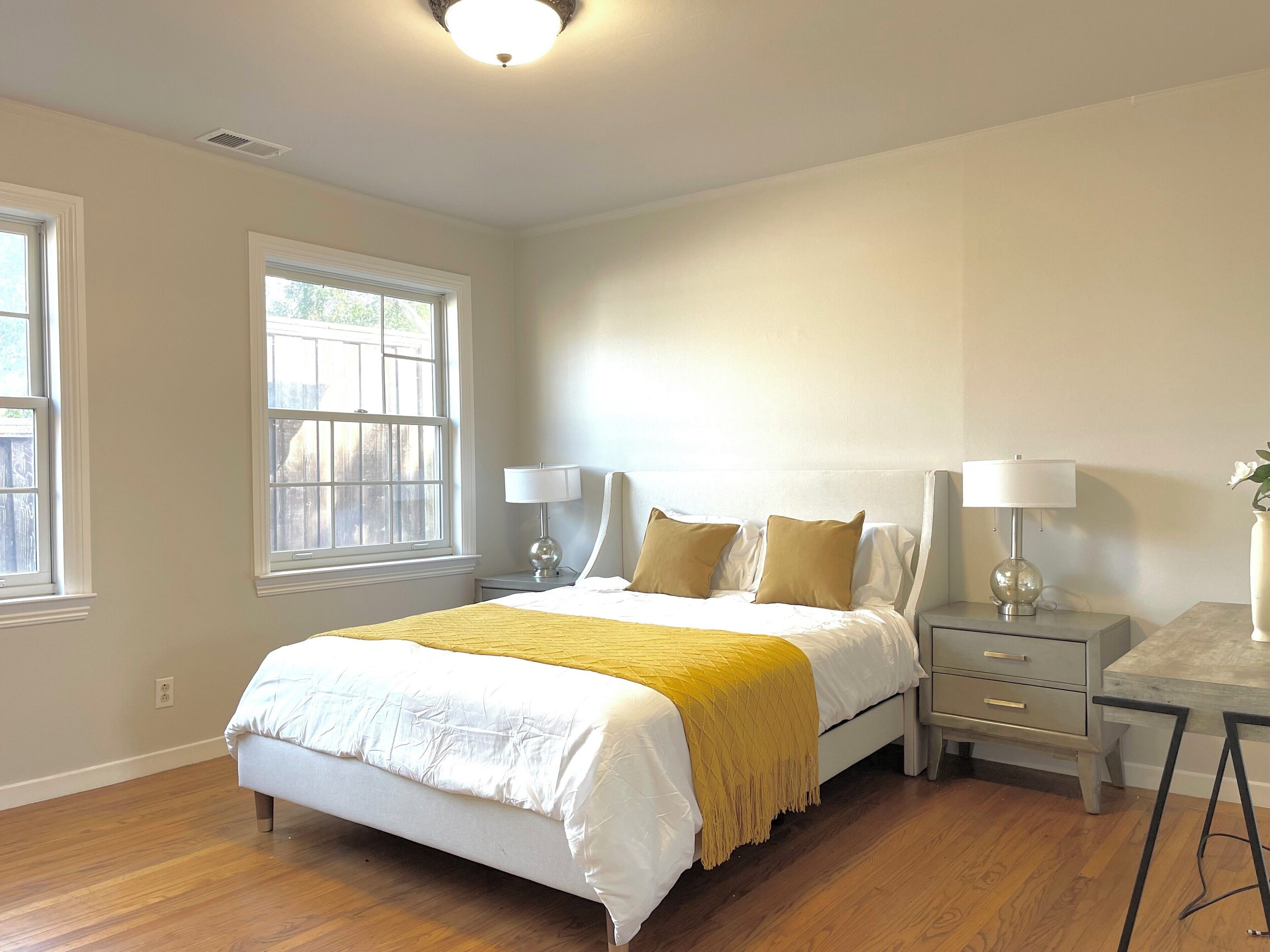 Une chambre à coucher avec un lit, deux tables de chevet avec des lampes, une fenêtre et un plancher en bois.
