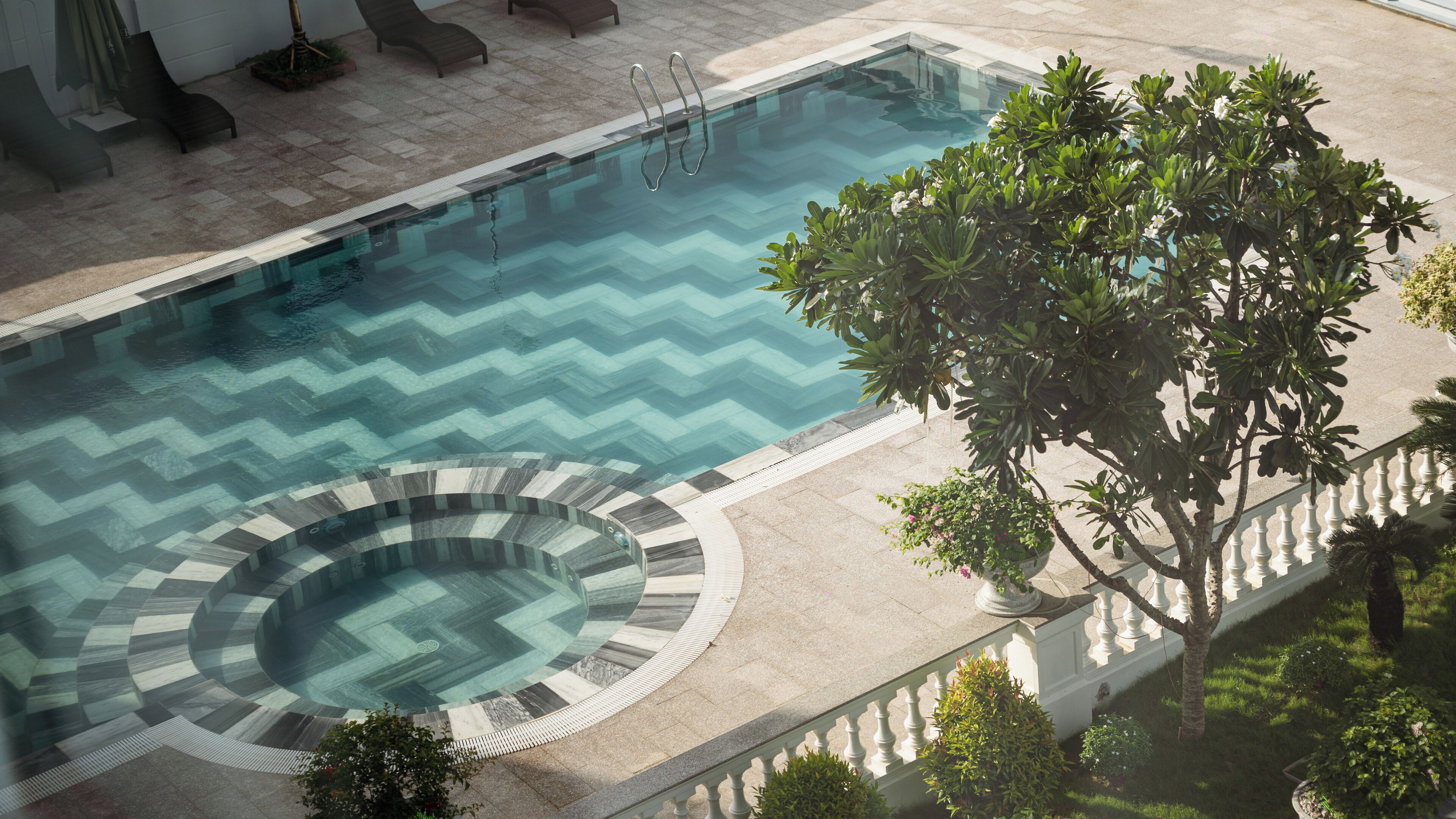 En swimmingpool med et gulethårsmønster, et spabad og frodig vegetation omkring.