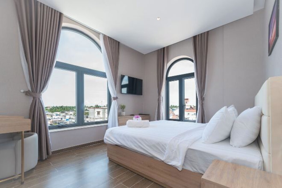A hotel room with a bed, a TV, and large windows with curtains.