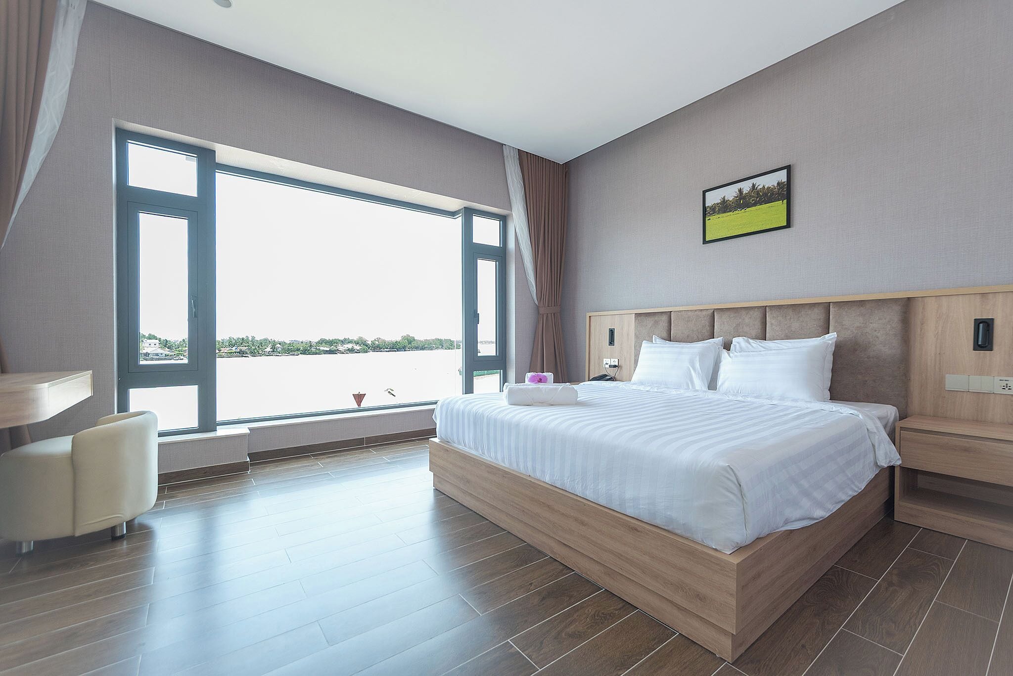 Habitación de hotel moderna con una cama grande, un escritorio y vista a una masa de agua a través de un ventanal amplio.