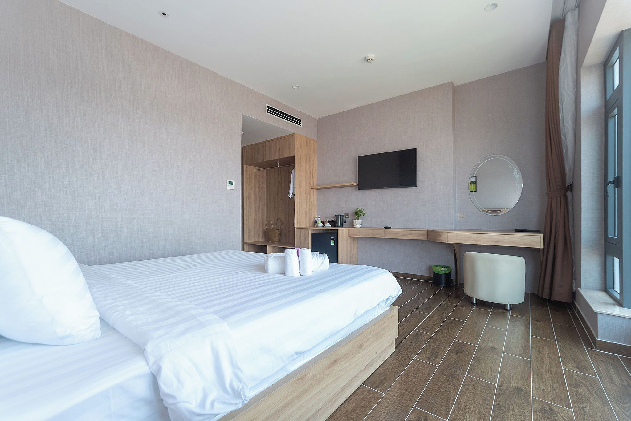 A modern hotel room with a large bed, a desk with a mirror, and a TV.