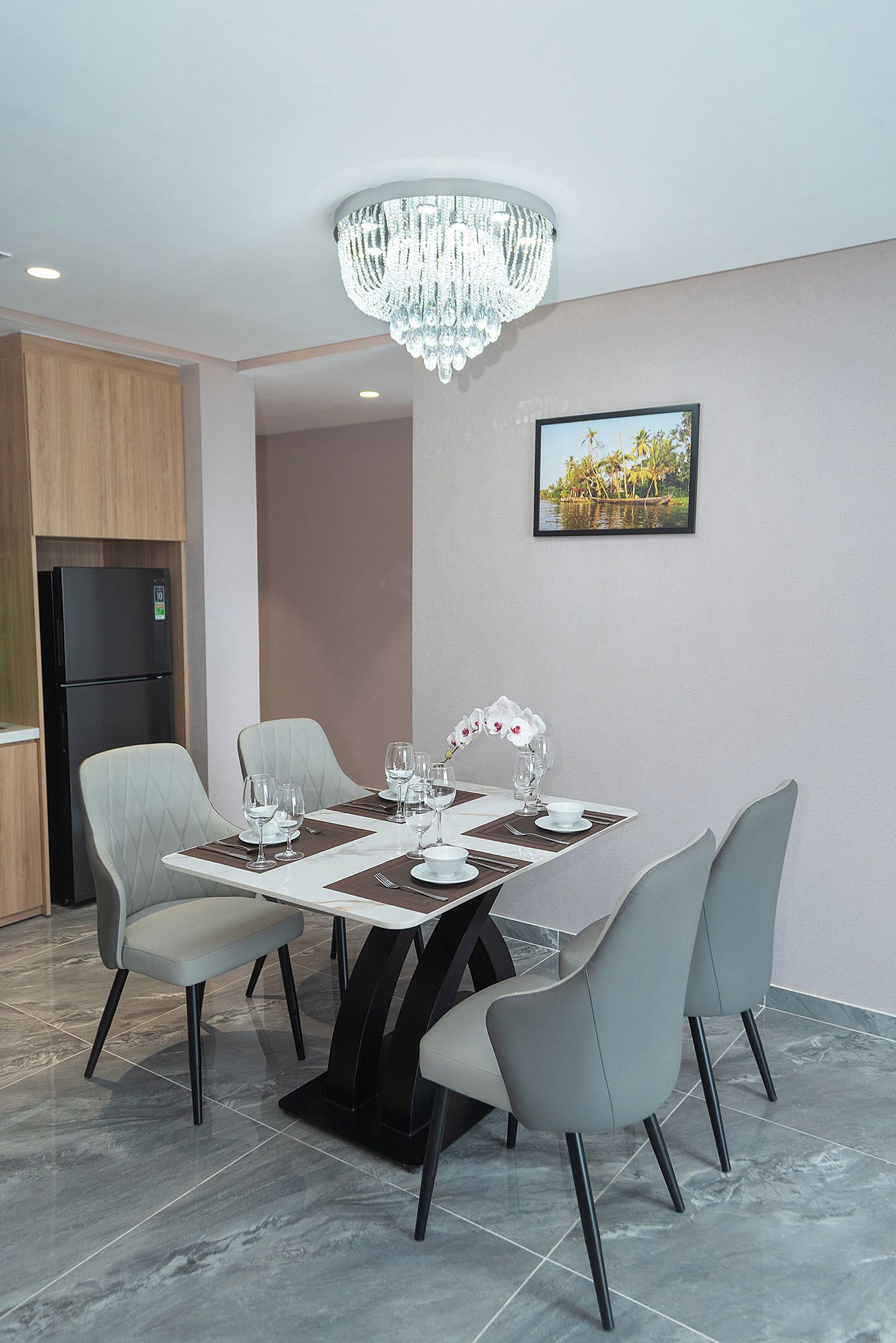 Un comedor con una mesa preparada para cuatro personas, sillas alrededor, una araña y un refrigerador al fondo.
