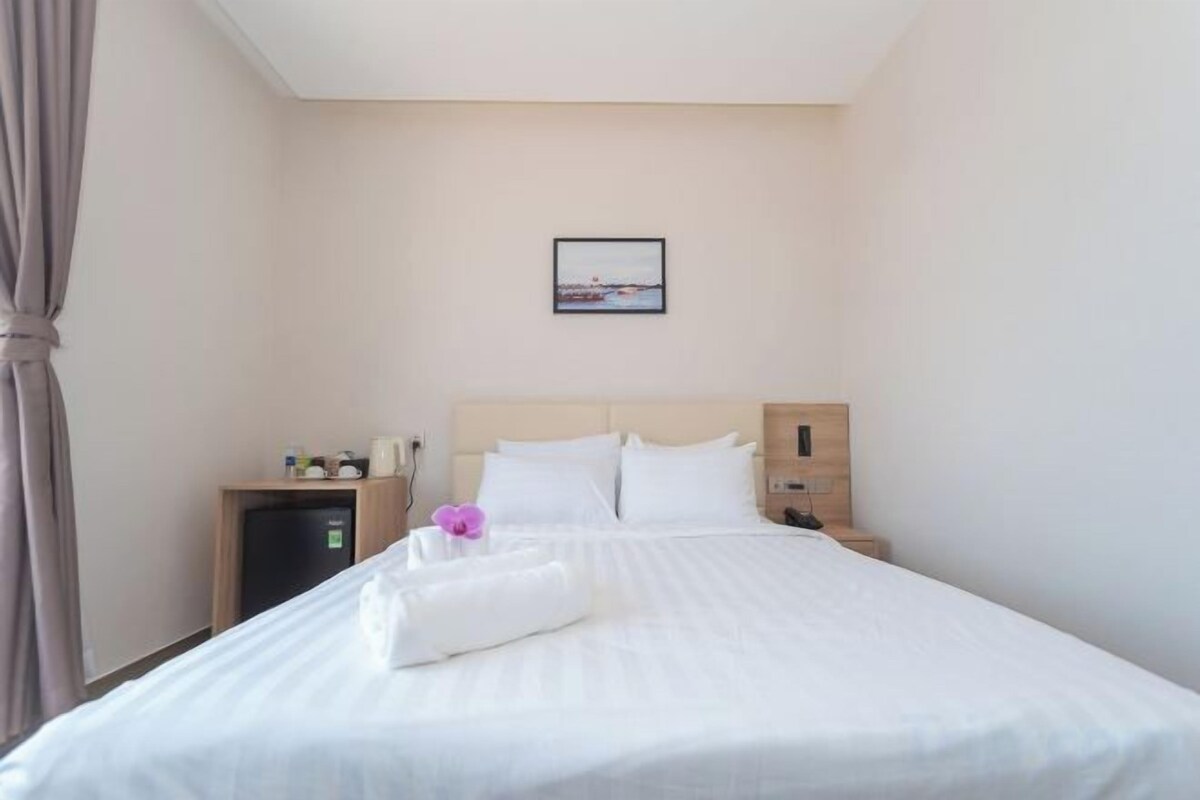 A hotel room with a bed, a nightstand, a small desk, and a wall-mounted picture.