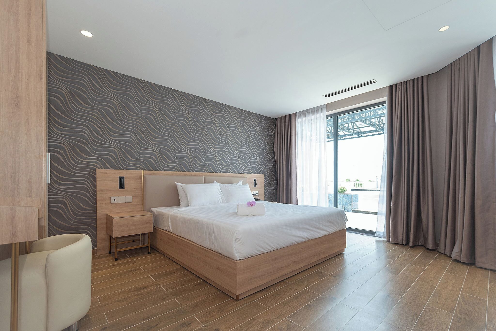 Ein modernes Hotelzimmer mit einem großen Bett, einem Nachttisch und einem Fenster mit Vorhängen.
