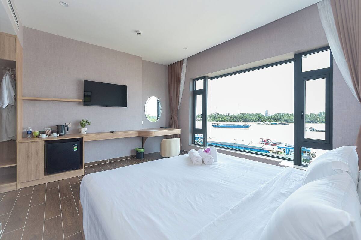 Camera d'albergo con un letto, televisione, mini-frigo, scrivania e finestra con vista sull'acqua.
