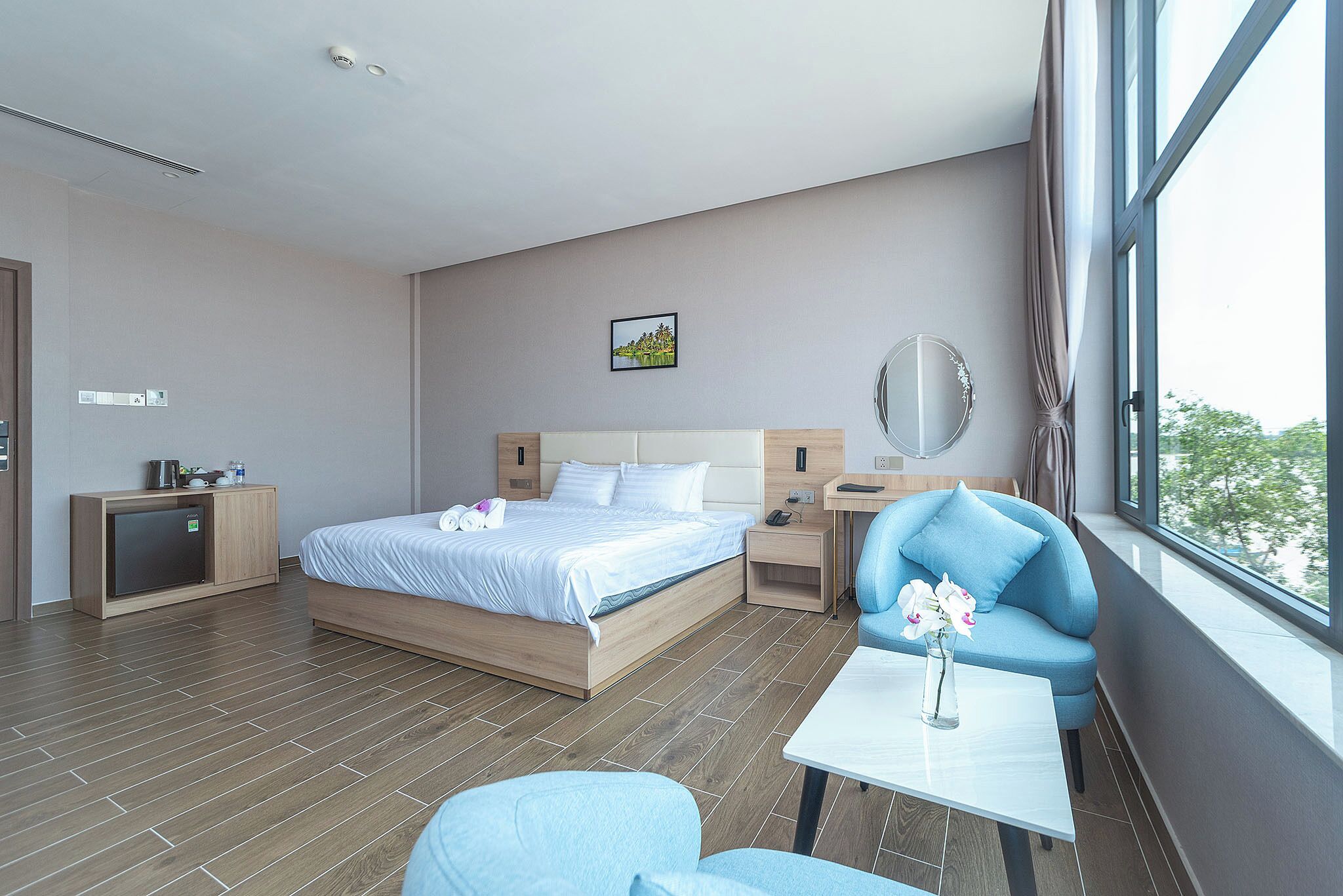 A modern hotel room with a bed, a small desk, a chair, a table, and a view of the outdoors.