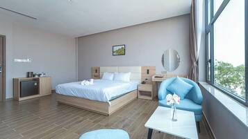 A modern hotel room with a bed, a small desk, a chair, a table, and a view of the outdoors.