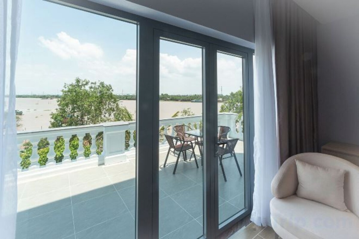 A balcony with a view of a river and trees, a sofa, and a table with chairs.