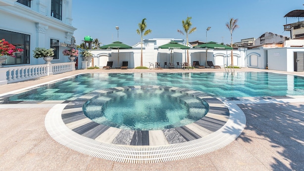 Una piscina de diseño circular, rodeada de sillones de descanso y sombrillas, y un edificio con fachada blanca y amplias ventanas.