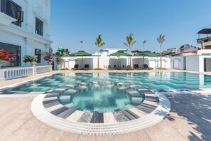 A swimming pool with a circular design, surrounded by lounge chairs and umbrellas, and a building with a white facade and large windows. - Bamboo Riverside Boutique Hotel (Phu Tuc)