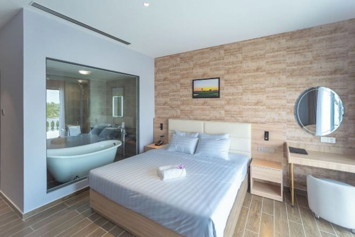 A modern hotel room with a large bed, a separate bathroom with a bathtub, a desk, and a large mirror.