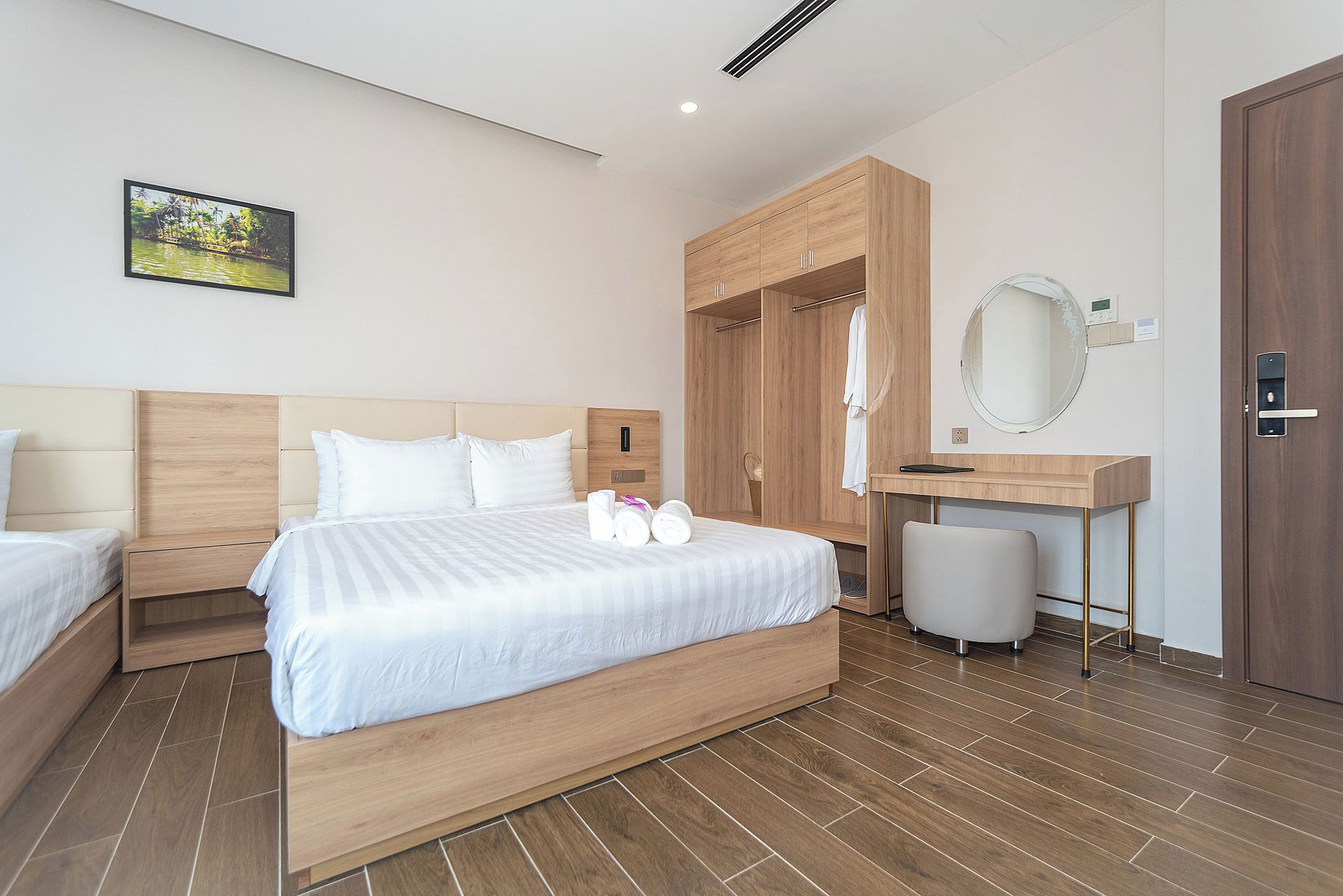 A modern hotel room with a large bed, a wooden wardrobe, a small desk, and a round mirror.
