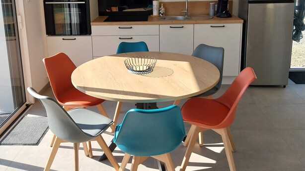 Una cocina moderna con una mesa redonda de madera, sillas coloridas, electrodomésticos integrados y un amplio ventanal.