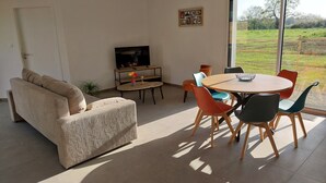 Una sala de estar moderna con un sofá, un televisor, una mesa de comedor con sillas y un ventanal con vistas a un paisaje verde.