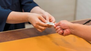A person handing over a small item to another person at a table. - nanbuhotel (Kitakami)