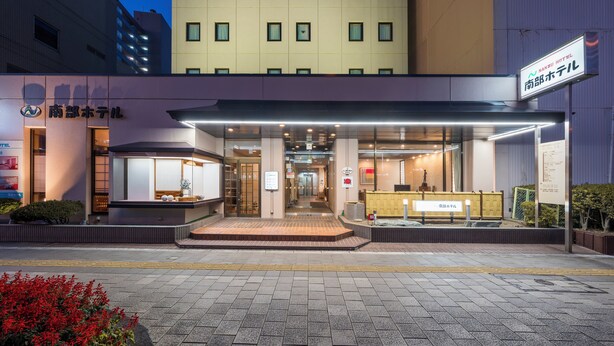 A hotel entrance with a covered walkway, a reception desk, and a sign indicating the hotel name. - nanbuhotel (Kitakami)
