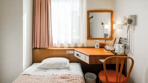 A hotel room with a bed, a desk with a telephone, a chair, a trash bin, and a window with curtains. - nanbuhotel (Kitakami)