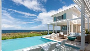 Un área de piscina con sillones de descanso y vista al océano.