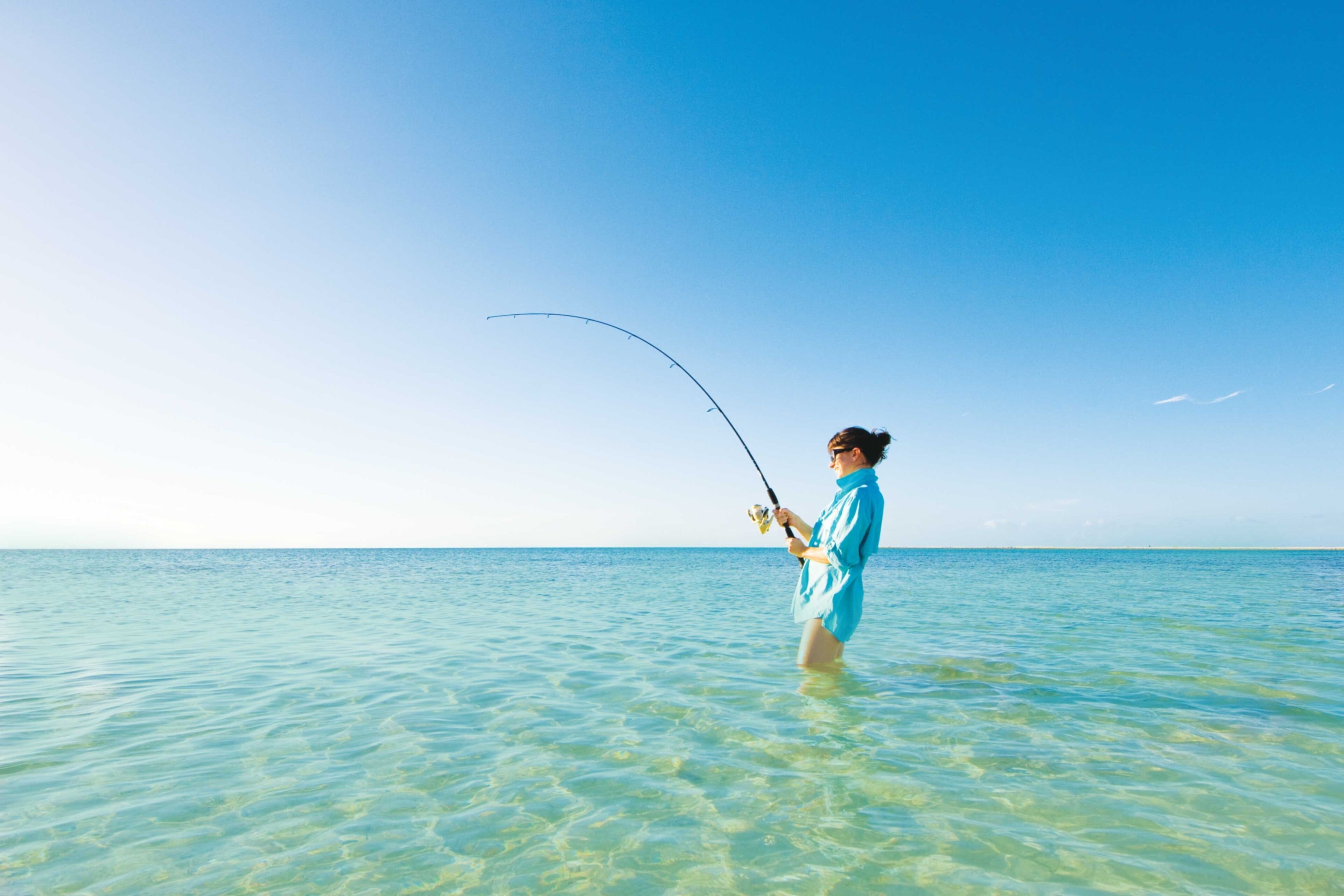 A person standing in shallow water holding a fishing rod.
