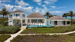 Una casa de dos pisos con piscina, rodeada de vegetación tropical y palmeras.