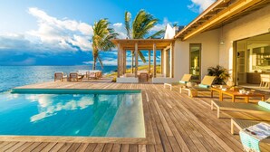 A wooden deck with a pool, outdoor seating, and a view of the ocean.