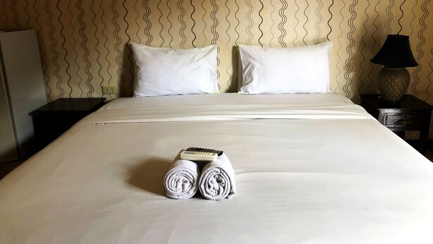 A neatly made bed with white linens, two pillows, and rolled towels on the bed.