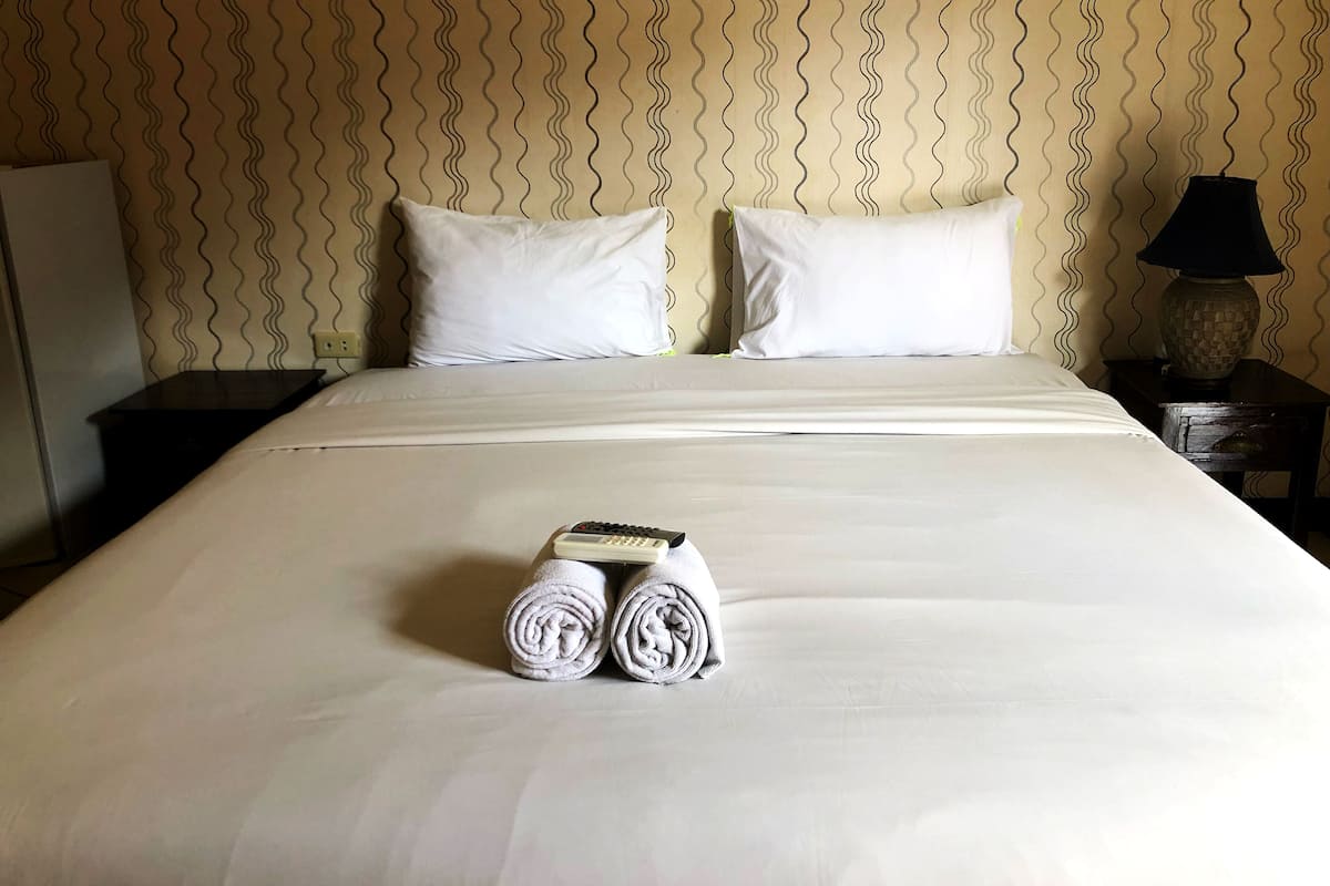 A neatly made bed with white linens, two pillows, and rolled towels on the bed.