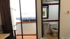 A hotel room with a balcony, a sink, a toilet, and a trash bin.