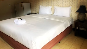 A hotel room with a neatly made bed, a small table with a lamp, and a refrigerator.
