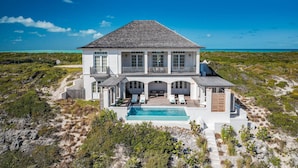 Une grande maison blanche avec une piscine, entourée d’une végétation luxuriante et offrant une vue dégagée sur l’océan.
