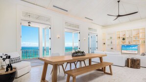 Un vaste espace de vie comprenant une table et des bancs en bois, des canapés blancs et un grand téléviseur.