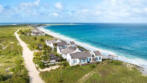 Une propriété située sur la côte, comprenant plusieurs bâtiments blancs, une plage de sable et offrant une vue dégagée sur l’océan.