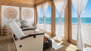 Une cabane en bois avec un coin repas, un canapé et une vue sur la plage.