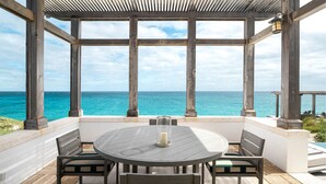 Un espace extérieur abrité, avec une table et des chaises, offrant une vue sur une mer turquoise.