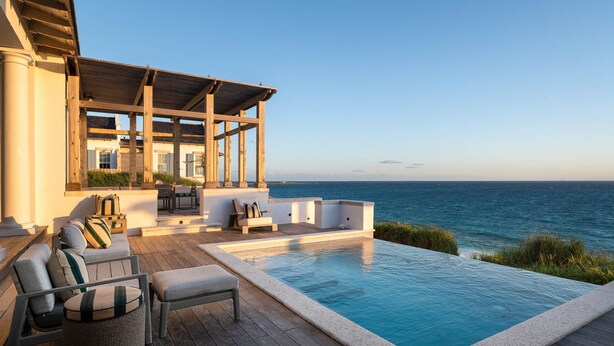 Zona junto a la piscina con terraza de madera, mobiliario exterior y vista al océano.