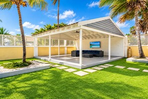 A covered outdoor seating area with a sofa and a television.